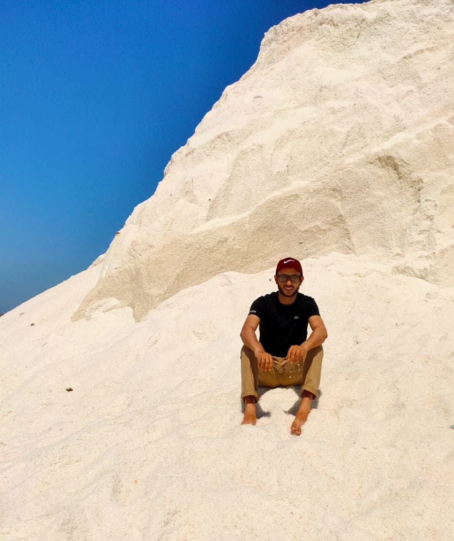 Khaled Arafa (Khalid Arafa) sitting on a white salt mountain outdoors, wearing sunglasses and a red cap